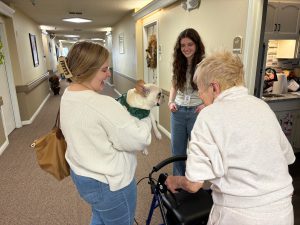 Emily holding her bulldog, Louis. She is showing Louis to a resident of an assisted living facility at which she is volunteering